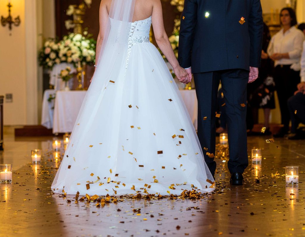 bride and groom walking down a candlelit aisle while gold confetti rains down